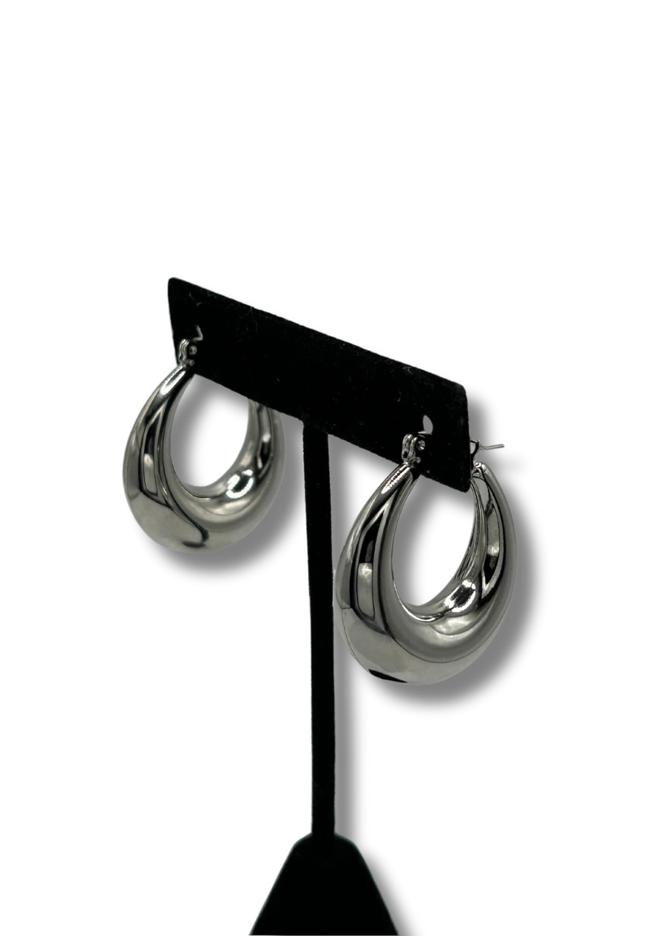 Large chunky oval stainless steel silver hoop earrings hanging on a black earring stand