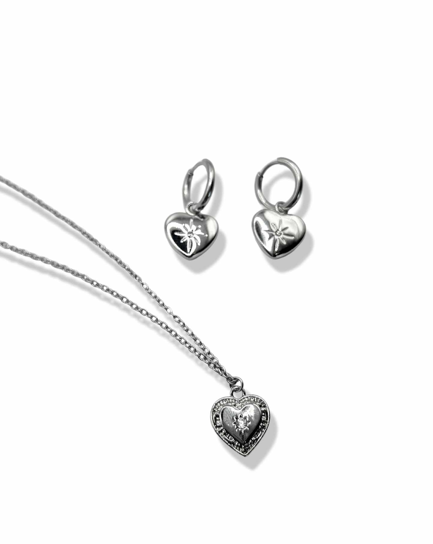 a dainty rhinestone star engraved heart pendant laying with matching heart huggie hoop earrings
