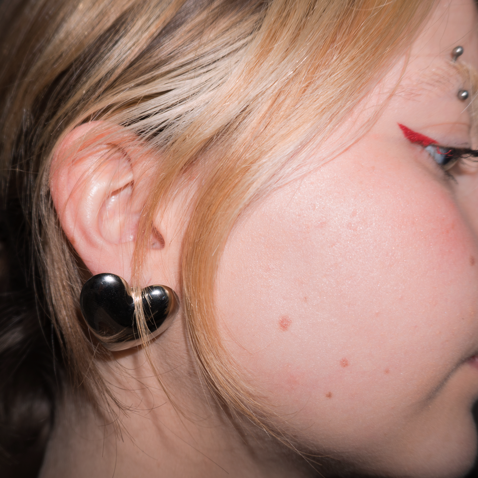Close up of a girl with blonde hair and red eyeliner wearing large stainless steel heart shaped stud earrings