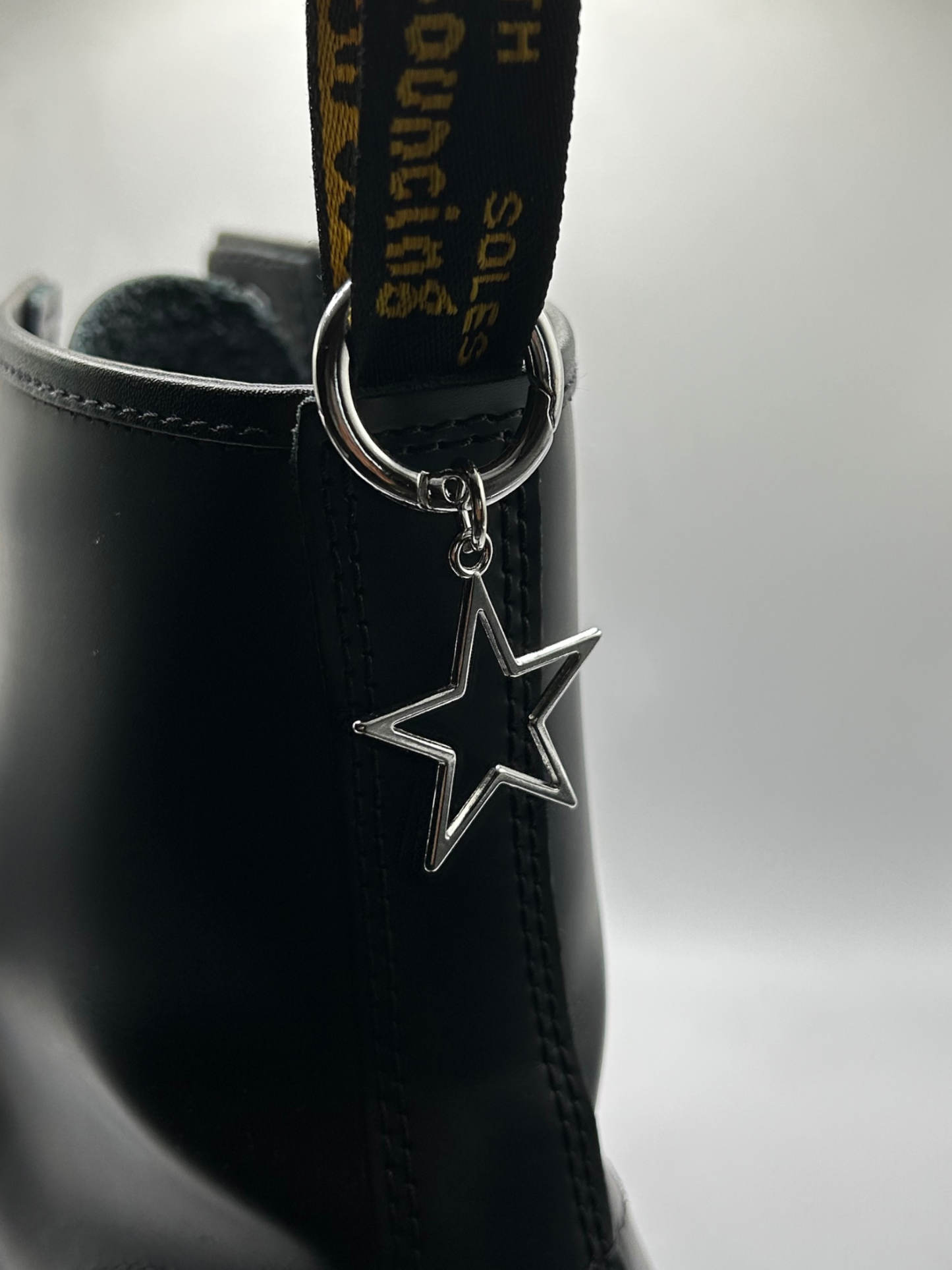 A black doc martens ankle boot with a hollow star pendant boot charm on the back looped through the tag