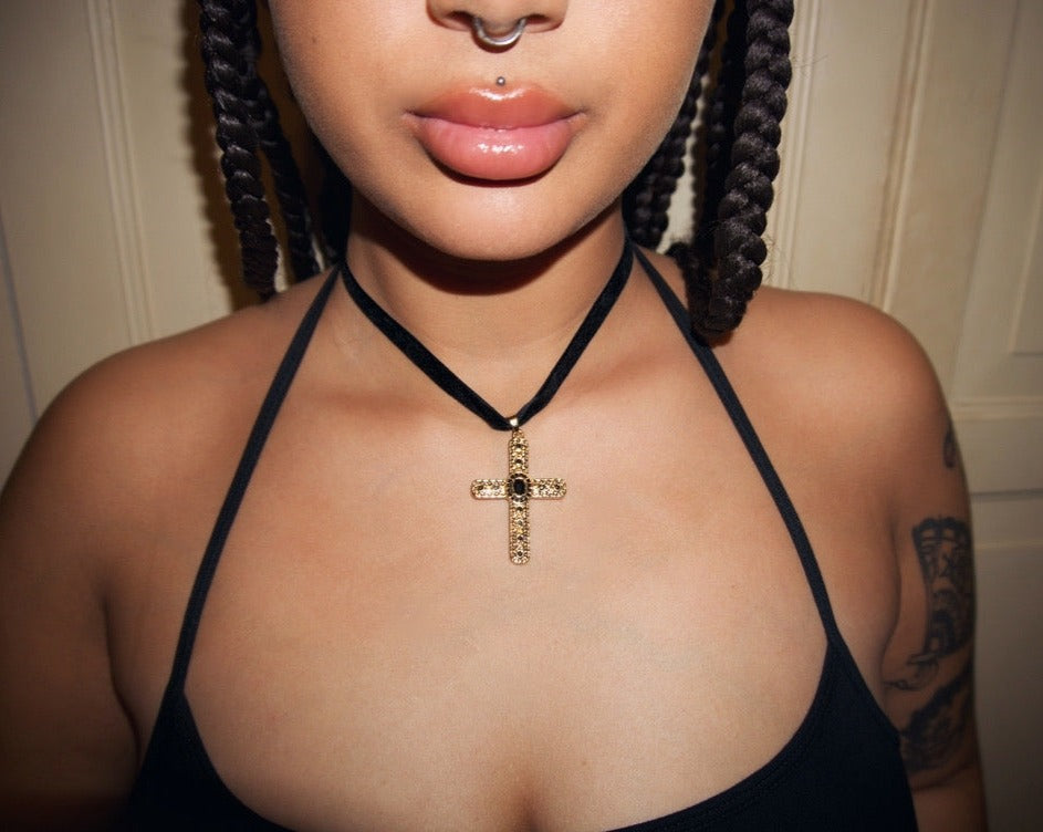 an up close shot of a girl with tattoos wearing a black velvet choker with a gold cross pendant adorned with black gems