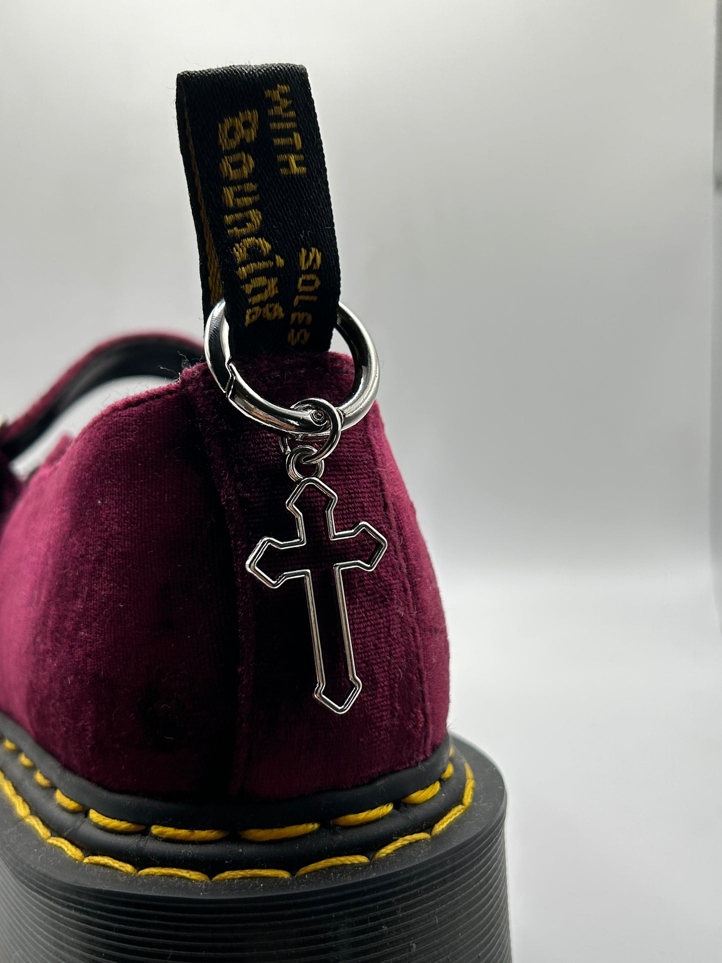 Burgundy velvet doc martens shoe with a stainless steel cross pendant boot charm on the back looped through the tag
