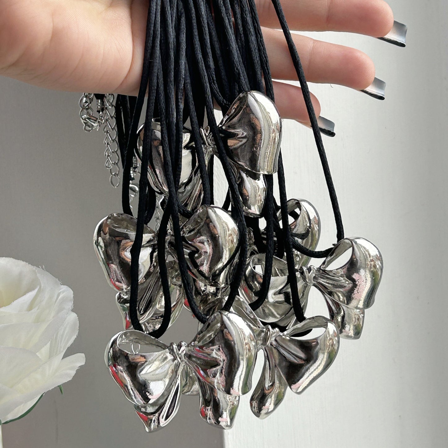 A hand with manicured nails holding multiple of the same chunky bow necklace next to a bouquet of flowers