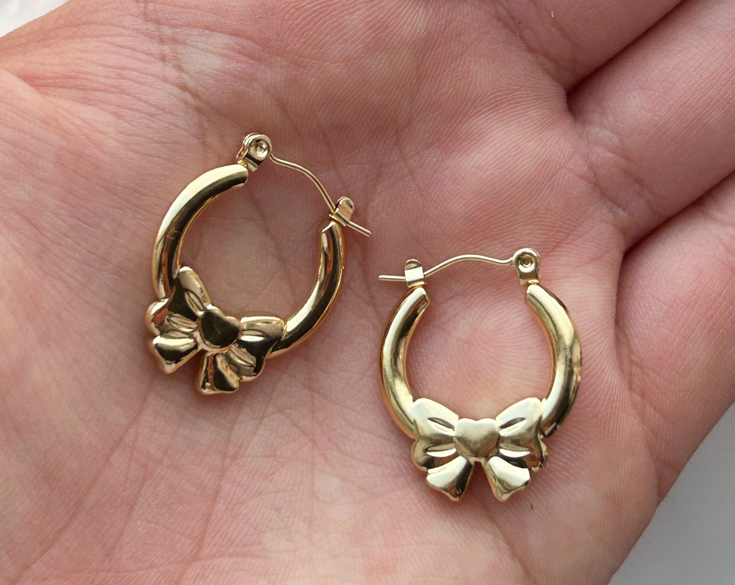 gold bow hoop earrings in the palm of someones hand