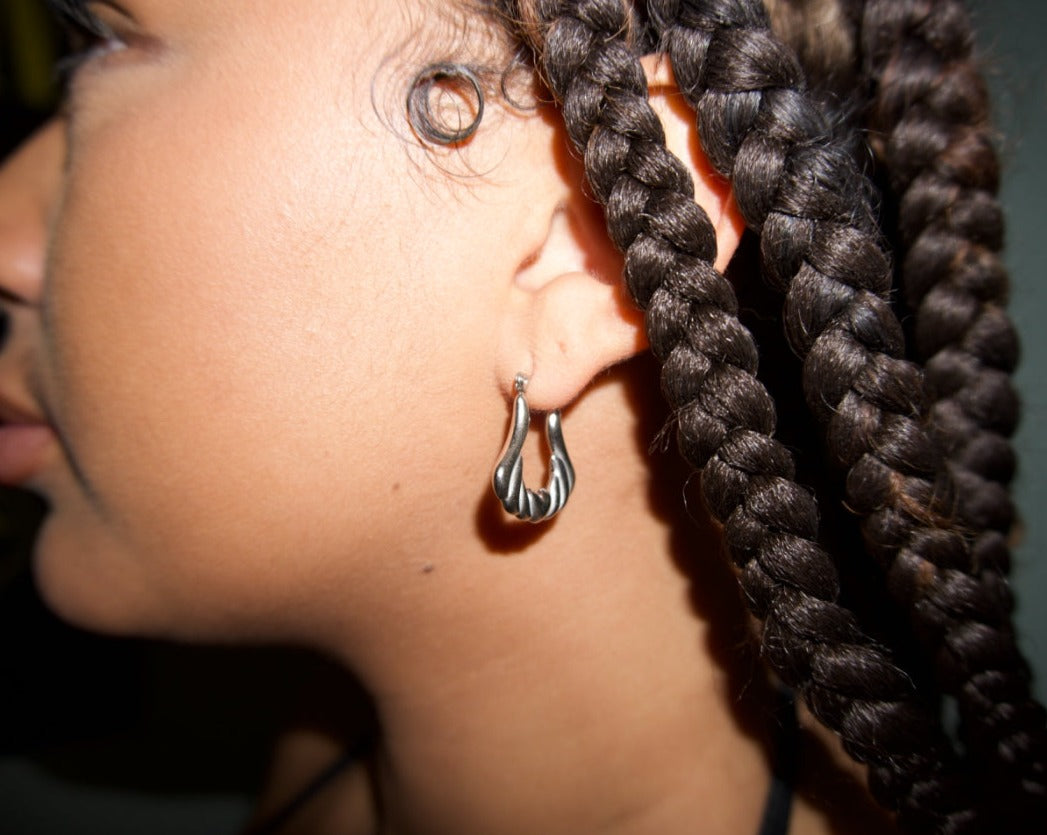 an up close shot of a girl with braids wearing silver stainless steel angel wing hoop earrings