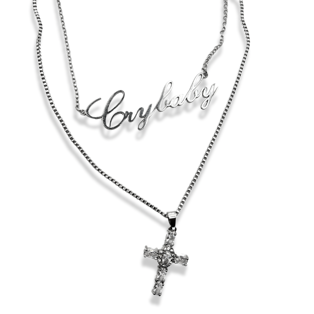 two necklaces layered together, one is a rhinestone cross pendant on a box chain and the other is a Crybaby nameplate necklace