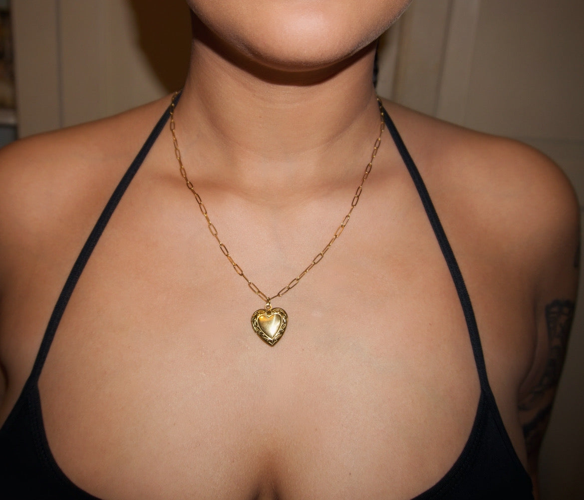 an up close shot of a girl with tattoos wearing a dainty gold chain with a detailed heart shaped locket pendant
