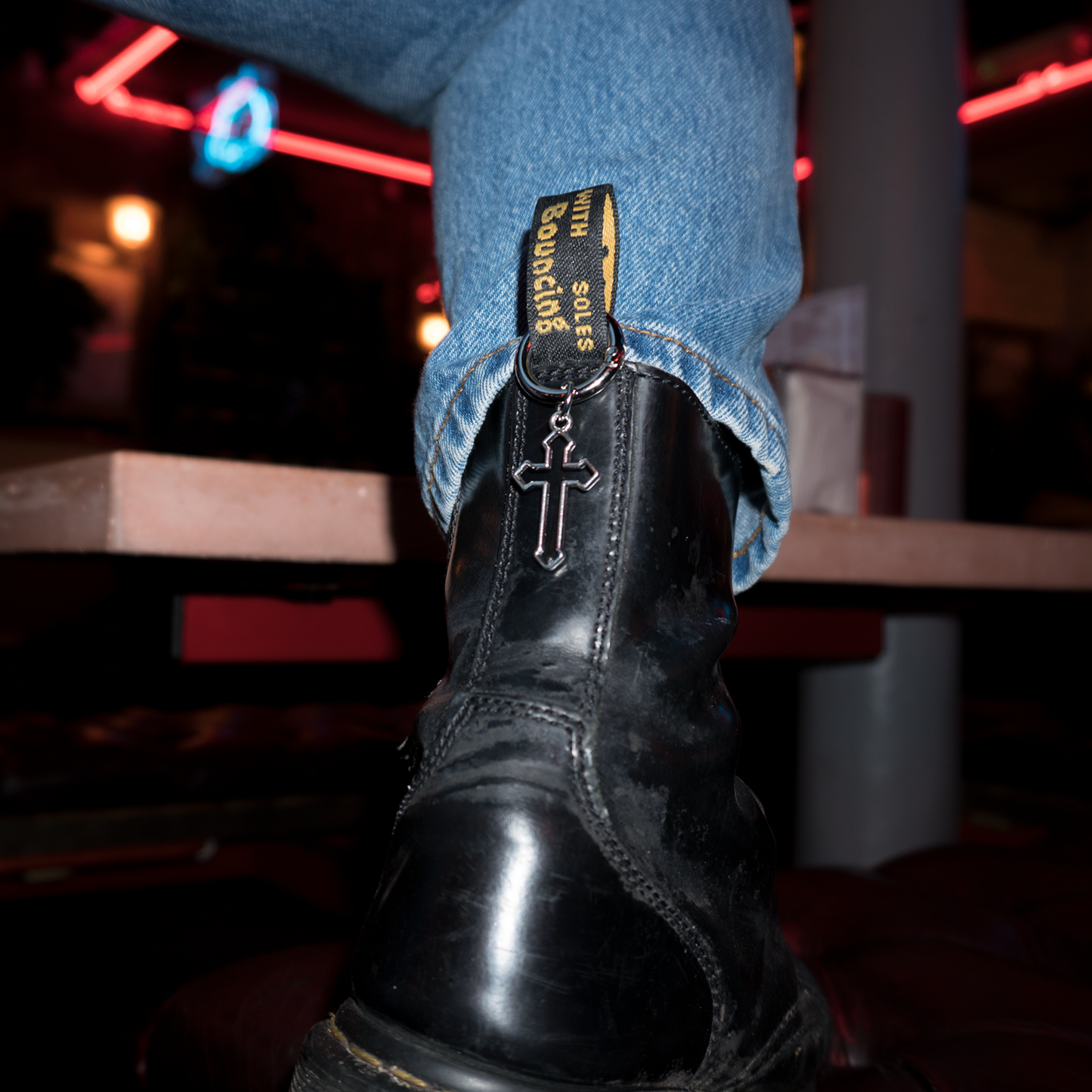 A close up image of a pair of doc marten boots, they have had a pendant added to the pull string on the back featuring a silver gothic style cross