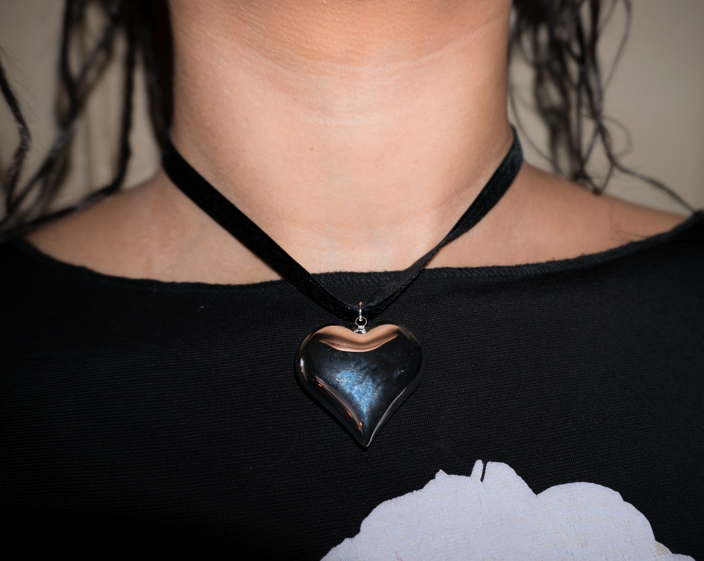 Silver heart pendant on a black ribbon necklace on a woman’s neck with a black flowery top