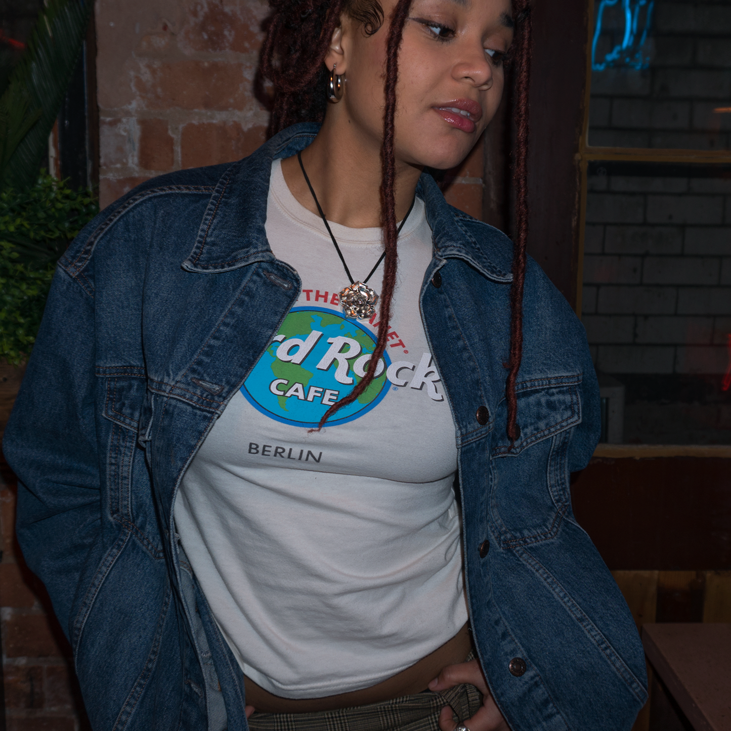 Shot of model wearing a denim jacket over a white shirt, with a chunky, silver metal rose pendant on her neck