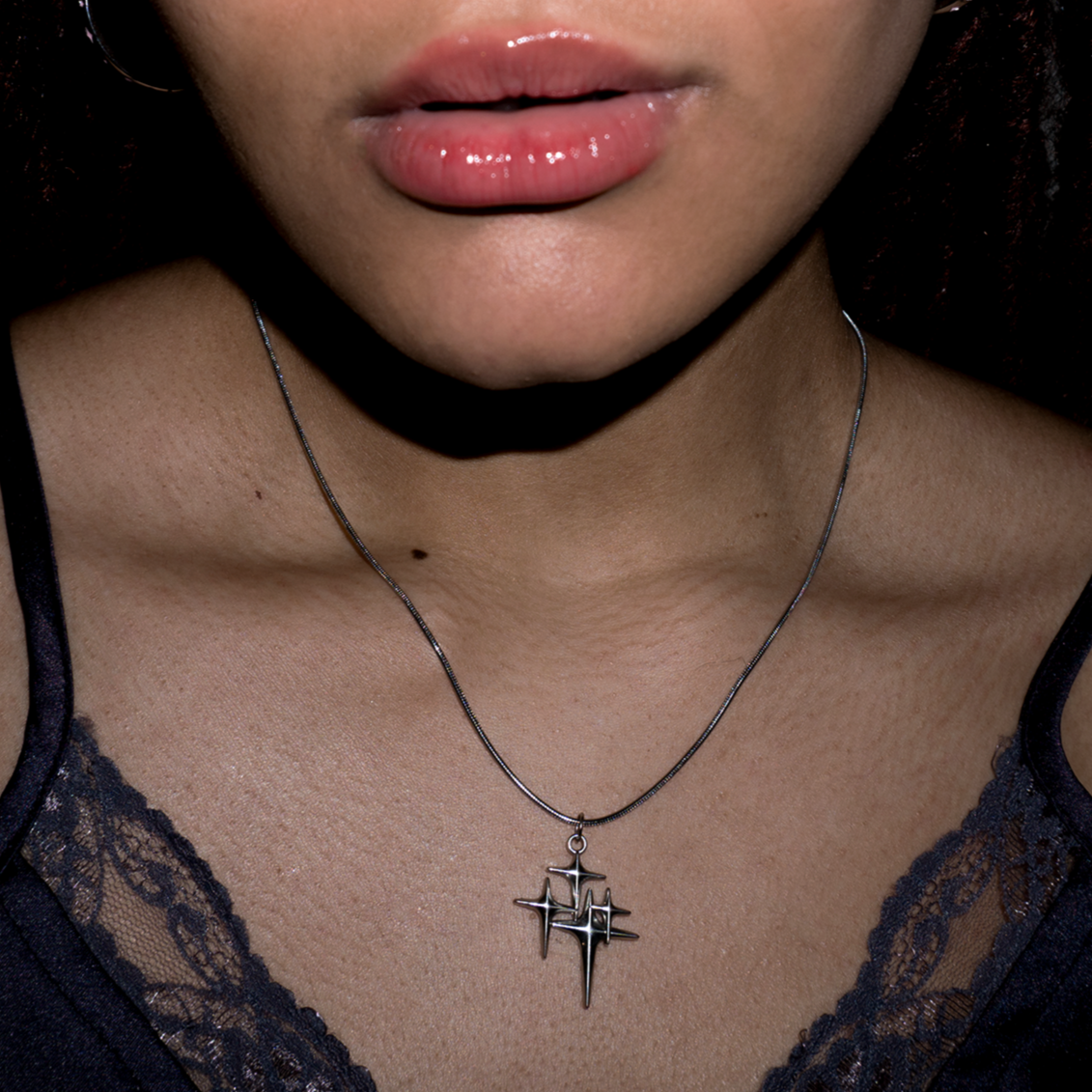 Close up of top of models chest with the stargirl necklace resting on her. The necklace is 4 small stars sparkling on a silver metal chain.