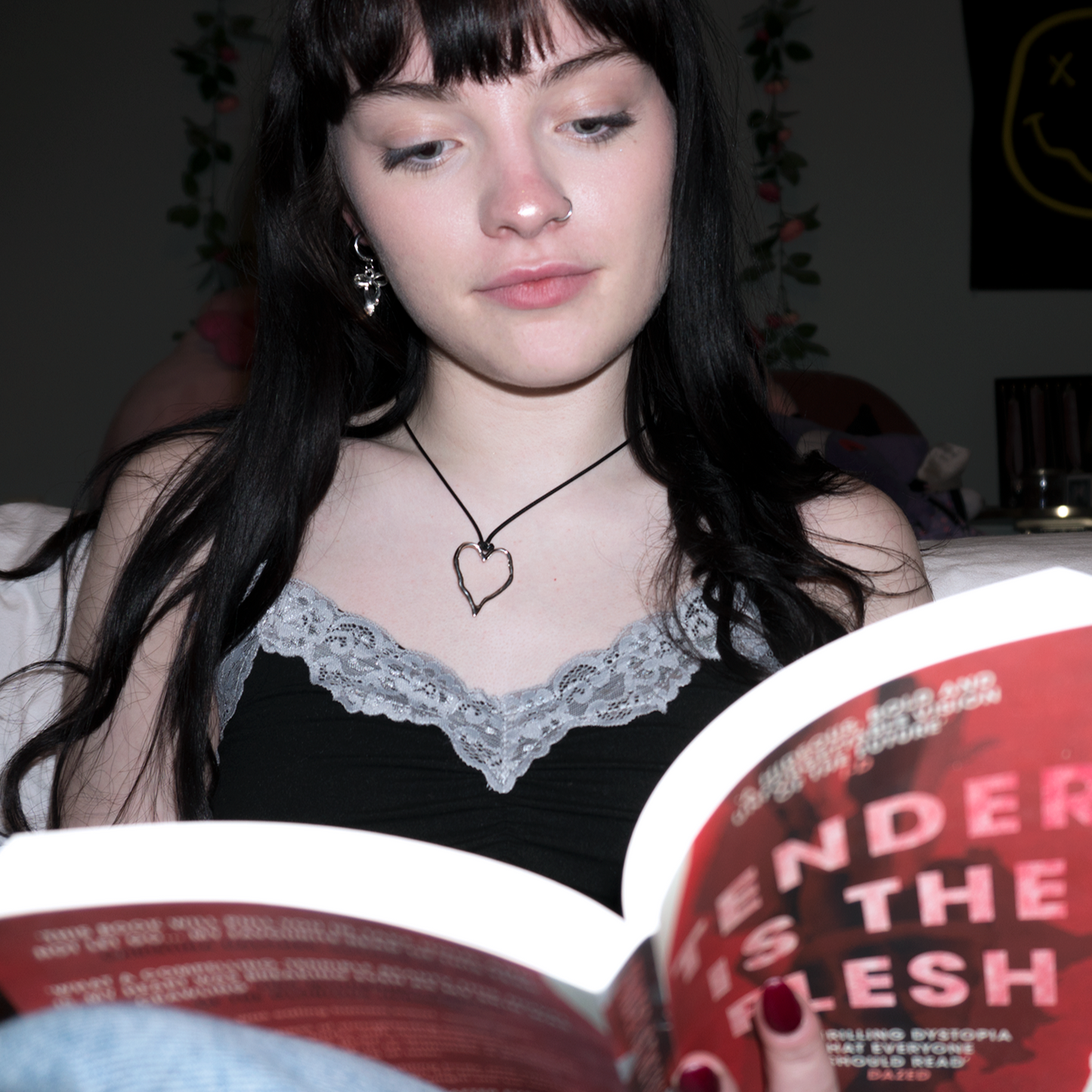 girl with long black hair reading a book, she is wearing a hammered heart shaped pendant on a black leather cord chain