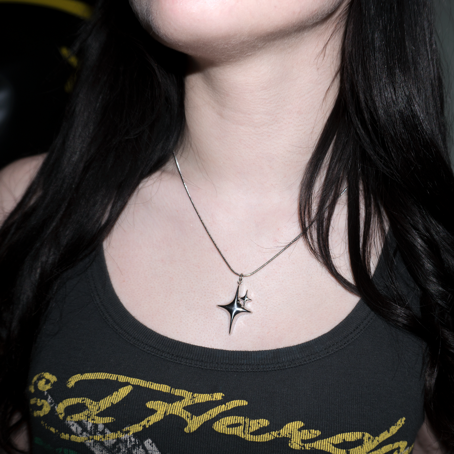 a girl with black long hair is wearing the stargirl XL, a large silver sparkle pendant necklace on a snake chain