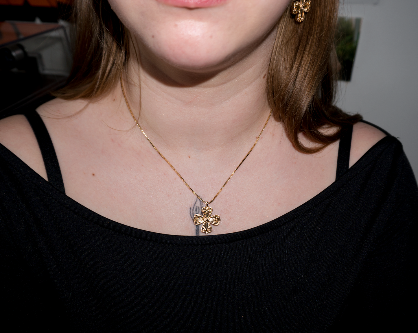 a girl with blonde hair wearing a gold clover/cross pendant necklace with matching earrings