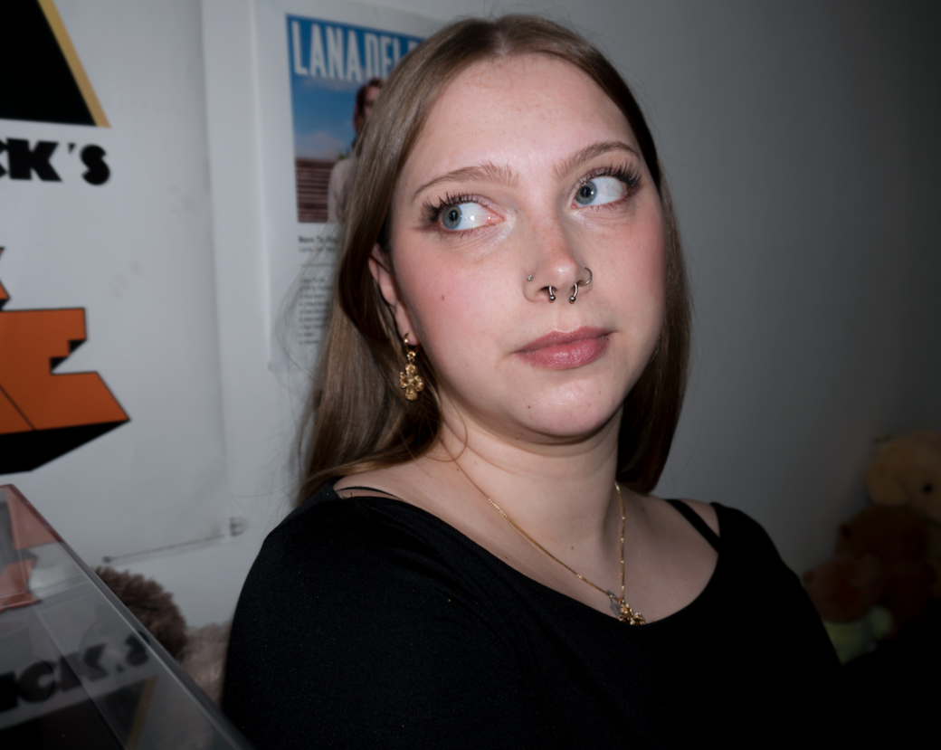 a girl with blonde hair wearing a gold clover/cross pendant necklace with matching earrings