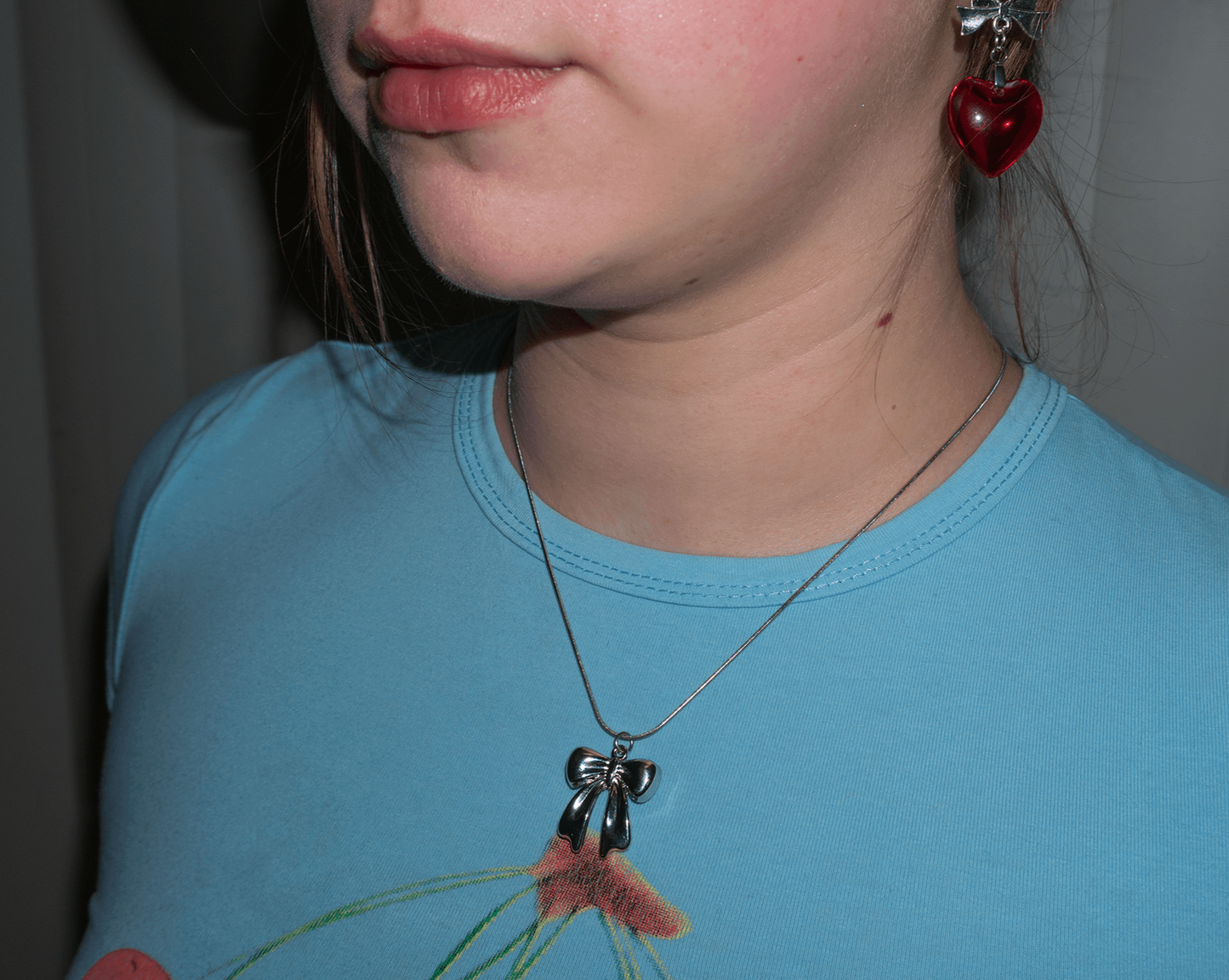 A close up of a womans neck wearing a small silver bow that looks like its made of ribbon, on a metal chain