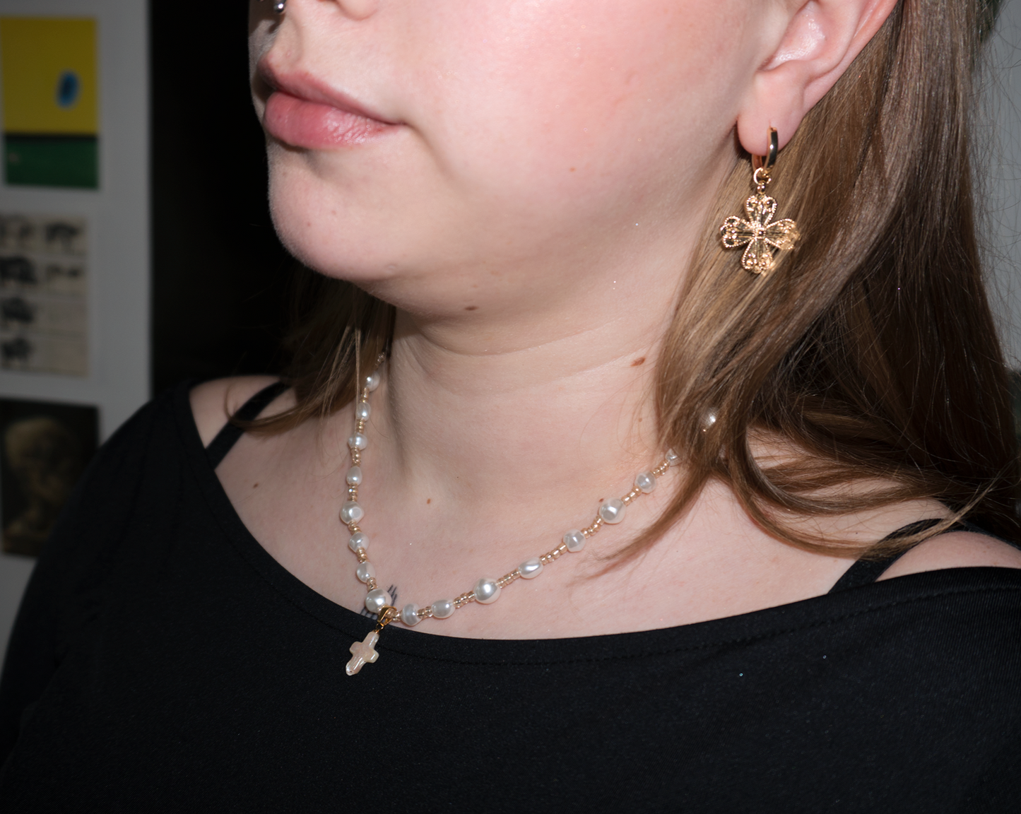 a girl with blonde hair wearing a freshwater pearl gold rosary necklace with a pearl cross pendant. she is also wearing gold clover/cross earrings
