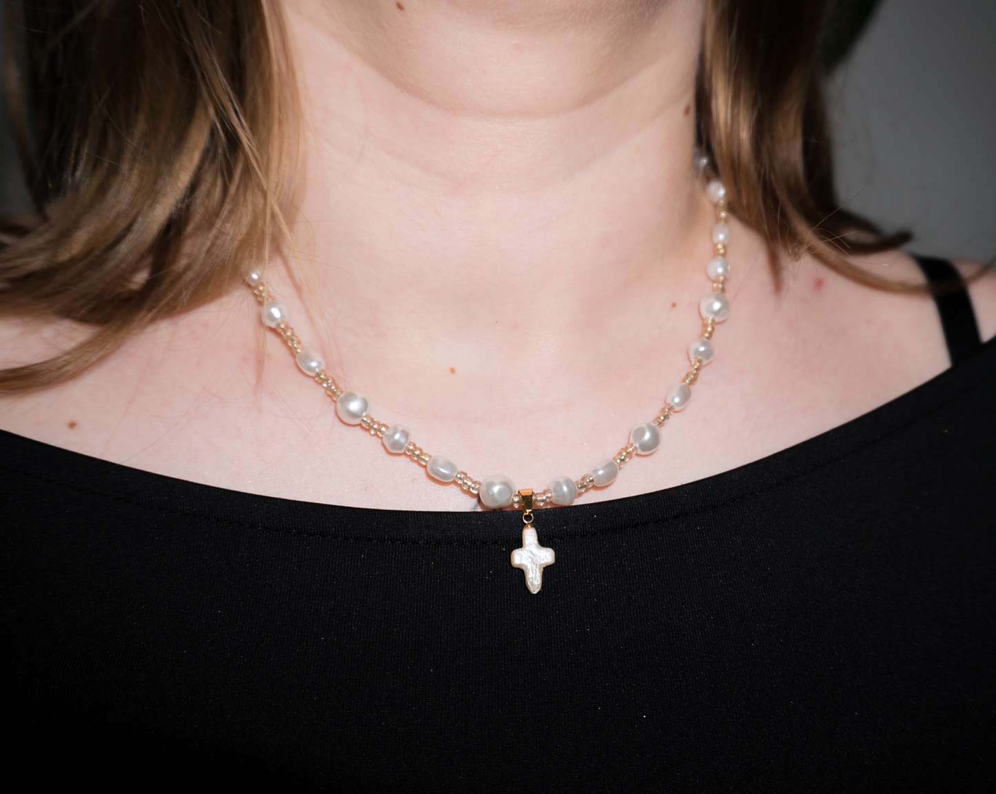 a girl with blonde hair wearing a freshwater pearl gold rosary necklace with a pearl cross pendant