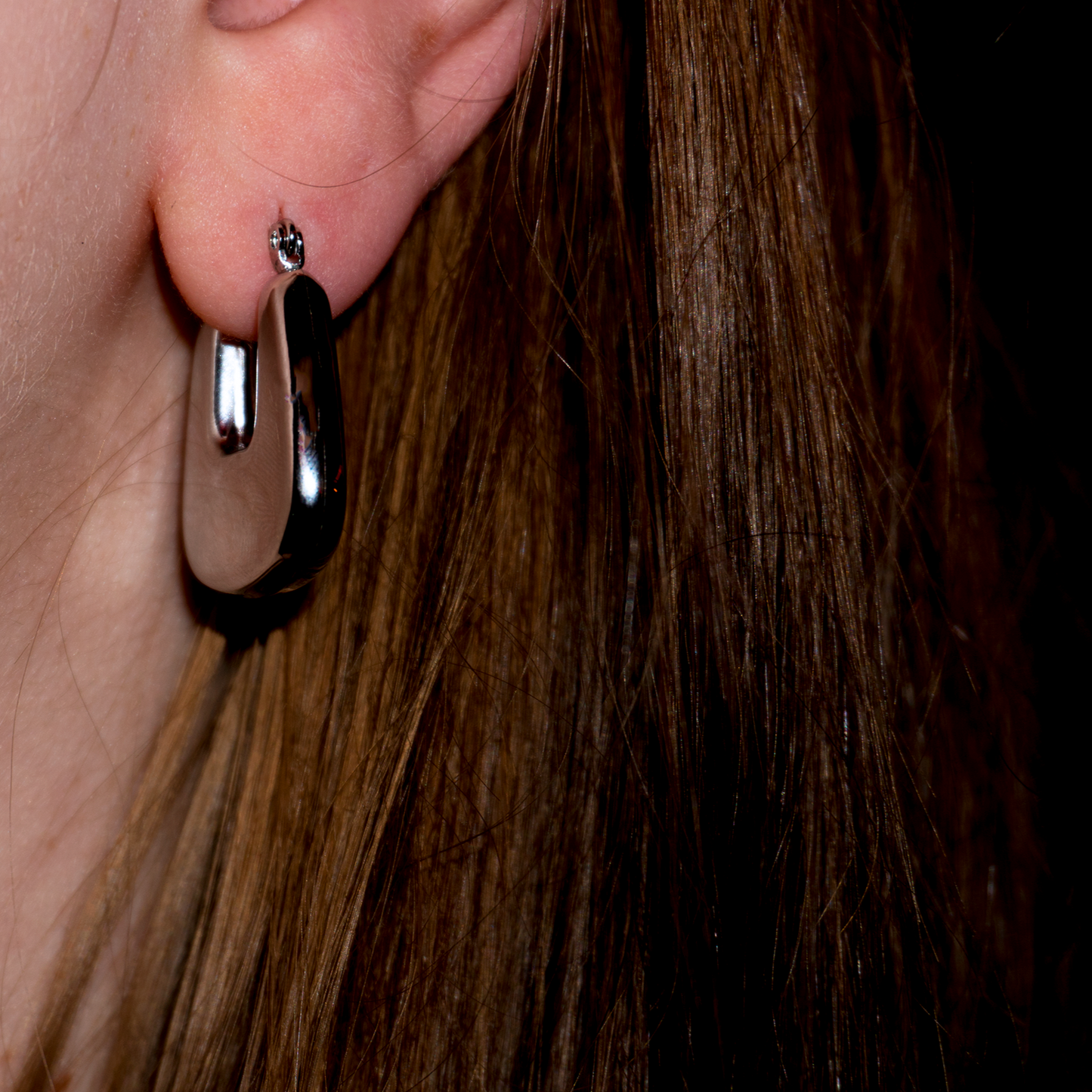 Extreme close up of a models ear wearing the Rae hoops earring, a chunky silver hanging pendant