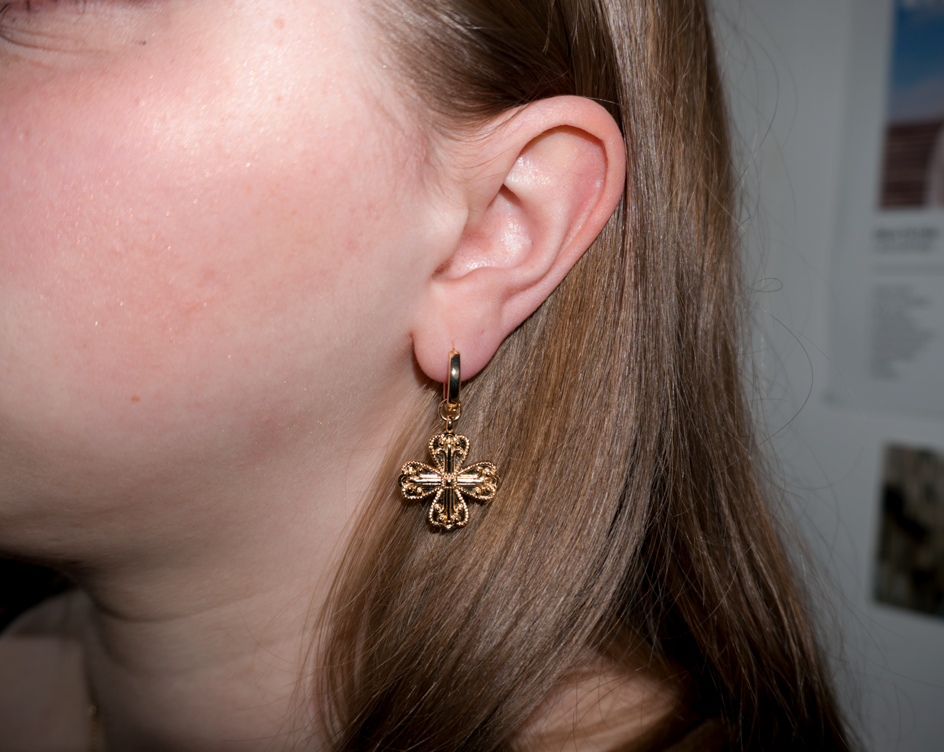a girl with blonde hair wearing dangly cross/clover gold earrings