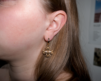 a girl with blonde hair wearing dangly cross/clover gold earrings