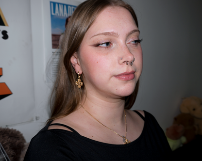 a girl with blonde hair and piercings, she's wearing dangly cross/clover gold earrings and a matching necklace